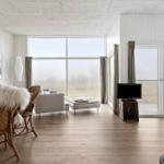 Wohnzimmer mit großem Fenster, Holzboden und Kamin. Möbel sind modern und schlicht.