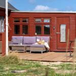 Roter Holzhaus mit Terrasse, Sofa, Grill und Sitzgelegenheiten.