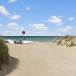 Sandweg führt zum Strand mit Blick auf das Meer und einen Verkehrszeichenpfosten.