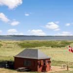 Rotes Holzhaus mit Terrasse, Blick auf Wasser und Dünen. Daneben steht eine Flagge.
