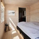 Schlafzimmer mit Holzwand und Bett. Fenster, Bild und Stuhl sind sichtbar.