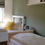 Zwei Betten mit weißen Bettwäschen und einem gelben Kissen. Grüne Wand und Fenster mit Blick nach draußen.