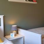 Zwei Betten mit weißen Rahmen und gelben Kissen. Zwischen ihnen steht ein Nachttisch mit Lampe.