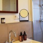 Bad mit Dusche, Waschbecken und Spiegel. Auf der Ablage stehen Seifen und ein Kerzenhalter.