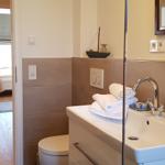 Badezimmer mit Waschbecken, Spiegel und Toilette. Handtücher und Seife sind vorhanden.