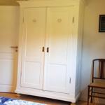 Schlafzimmer mit weißen Schrank, Holzstuhl und Lampen.