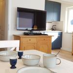 Esstisch mit Geschirr, Fernseher und Küchenbereich im Hintergrund.