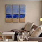 Wohnzimmer mit Sofa, Tisch und Wandbild. Fenster mit Blick nach draußen.