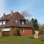 Ein zweistöckiges Haus mit rotem Dach und Garten. Ein Holzstuhl steht draußen.