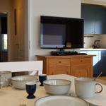 Esszimmer mit Tisch, Schüsseln und Kaffeetasse. Küche und TV im Hintergrund.