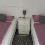 Zwei Einzelbetten mit rosa und grauen Kissen und einem weißen Nachttisch dazwischen.