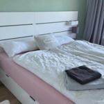 Schlafzimmer mit weißem Bett und rosa Matratzenrand. Fenster mit grauen Vorhängen.