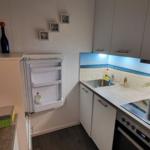 Küche mit Kühlschrank, Spüle und Herd. Oberflächen sind weiß. Wandbild mit blauem Licht.