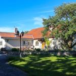 Haus mit rotem Dach, Garten und großer Baum. Terrasse mit Tisch und Stühlen.