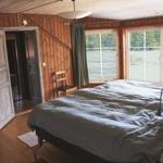 Schlafzimmer mit Bett, Fenstern und Holzwandverkleidung.