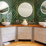Dusche mit grünen Fliesen, drei runden Spiegeln und zwei Waschbecken auf Holzoberfläche.