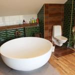 Bad mit freistehender Badewanne, Toilette und grünen Fliesen.
