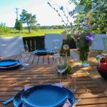 Rundtisch auf Terrasse mit Blumenvase, Weinflasche und Tomaten.