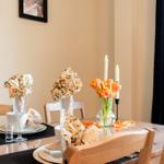 Gestellter Tisch mit Blumen, Kerzen und Geschirr. Holzstühle und dunkle Vorhänge.