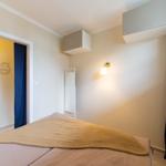 Schlafzimmer mit Bett, Wandlampe und Tür zum Badezimmer.