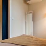 Schlafzimmer mit Bett, Spiegel und Wandlampe. Dunkelblaue Vorhänge und Wanddekoration.