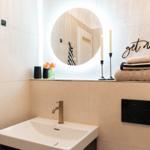 Badezimmer mit Waschbecken, runden Spiegel und Handtuchhalter.