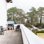 Terrasse mit Tisch, Stühlen und Strandkorb. Blick auf Bäume und Straße.
