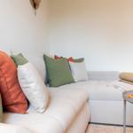 Ein Sofa mit Kissen in Grün und Orange. Tisch mit Kerze und Pflanze.