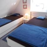 Zwei Einzelbetten mit blauen Decken und Kissen in einem Schlafzimmer mit Fenster und Nachttisch.