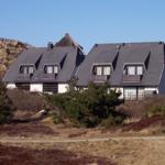 Moderne Ferienhäuser mit Balkonen und dunklen Dächern stehen in einer natürlichen Umgebung.