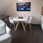 Essbereich mit Tisch, Stühlen und Wand-TV unter schräger Decke.