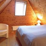 Schlafzimmer mit Bett, Sessel und Fenster unter Holzdecke.