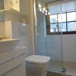 Badezimmer mit Dusche, Waschbecken und Toilette. Fenster mit Holzrahmen.