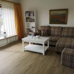 Wohnzimmer mit Sofa, Couchtisch und Bücherregal. Fenster mit Vorhängen und Blick auf Balkon.