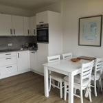 Küche mit Essbereich, weiße Möbel und Holzboden