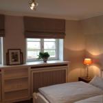 Schlafzimmer mit Bett, Nachttisch, Lampe und Fenster mit Pflanze.