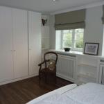 Schlafzimmer mit weißen Schränken, Holzboden und Fenstern mit Rollläden.