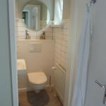 Badezimmer mit Toilette, Waschbecken und runden Spiegel. Handtuch hängt an Tür.