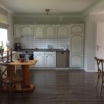 Küche mit weißen Schränken, dunklem Holzboden und Essbereich.