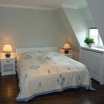 Schlafzimmer mit Dachschrägen, Bett mit blauem Bezug, zwei Nachttische und Fenster mit Pflanze.