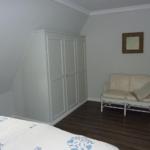 Schlafzimmer mit Dachschräge, Kleiderschrank, Sessel und Holzboden.