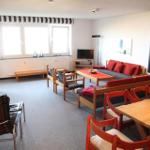 Wohnzimmer mit Sofa, Tisch und Stühlen. Fenster mit Streifenrollo.