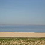 Strand mit Sandstrand und ruhigem Meer unter klarem Himmel.