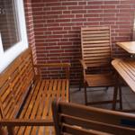 Terrasse mit Holzmöbeln, roter Ziegelwand und Blick auf Grünfläche.