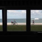 Durch Fenster blickt man auf Strand, Meer und Schiff.