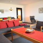 Wohnbereich mit Sofa, Tisch und Stühlen. Rote Kissen und Tischdecke.