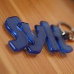 Blauer Schlüsselanhänger mit Buchstaben liegt auf Holzoberfläche.