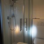 Duschkabine mit Glaswand, Toilette und Waschbecken im Badezimmer