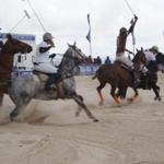Polo-Spieler reiten Pferde auf Sand und kämpfen um einen Ball.
