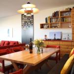 Essbereich mit Holztisch, roten Stühlen und Sofa. Wandregale und Lampen sichtbar.